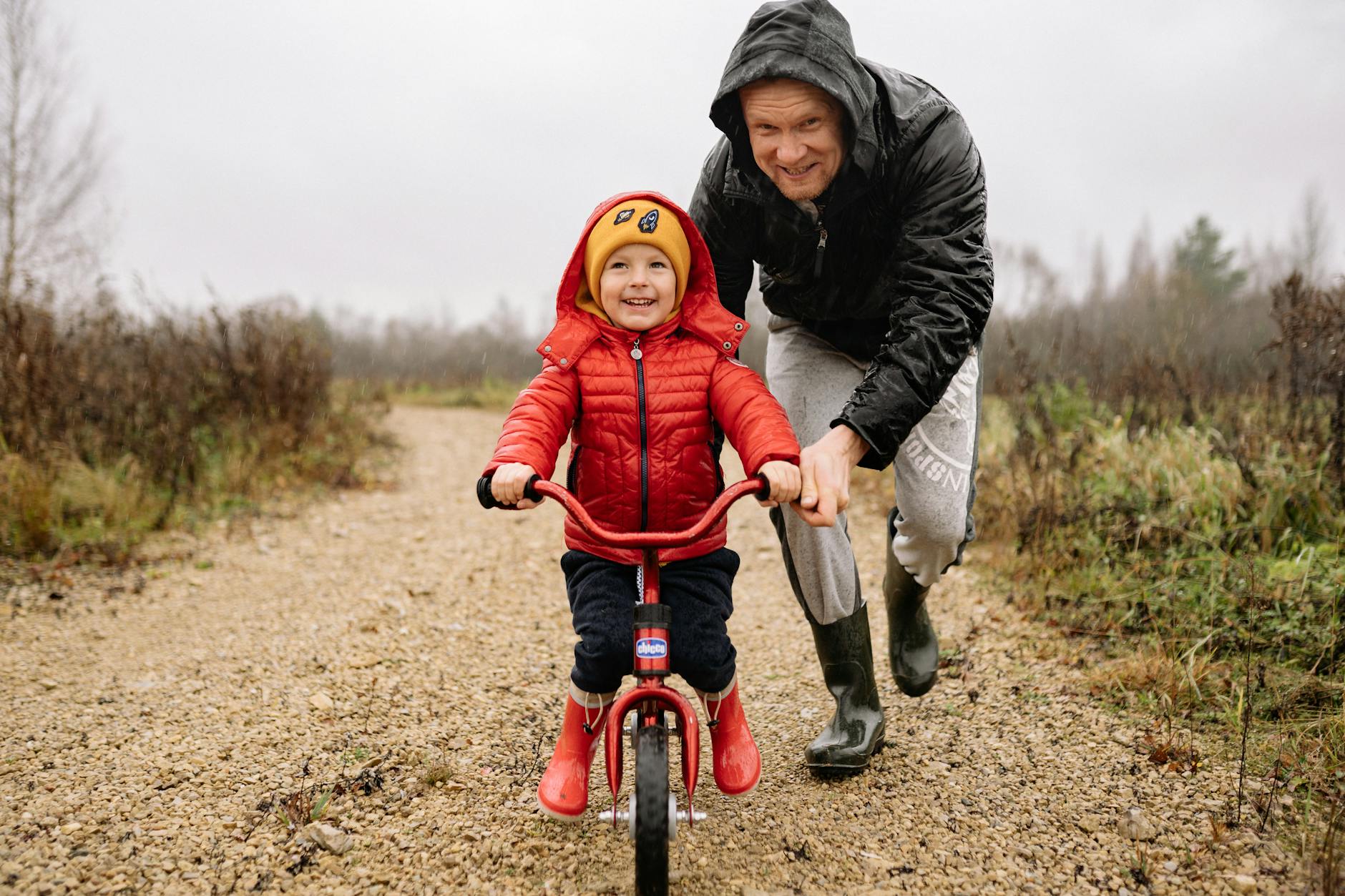 Dad teaching child in a red jacket how to ride a bike
